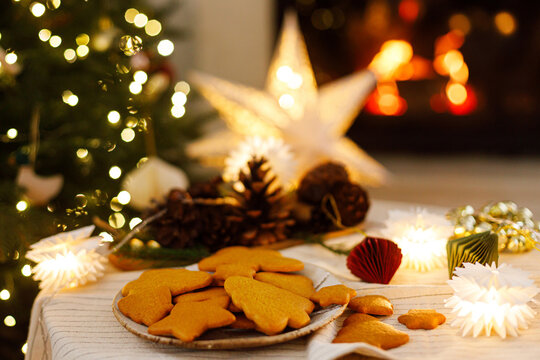 Delicious Christmas Gingerbread Cookies on Ceramic Plate with Warm Glowing Fireplace and Christmas Lights Background. Merry Christmas. Cozy xmas