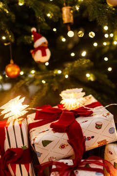 Cozy Christmas Gift Boxes Wrapped with Red Ribbons and Star Lights Under Illuminated Tree with Golden Bokeh Background. Happy holidays