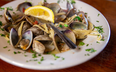 Clams linguine pasta served in a white wine garlic sauce, garnished with a fresh lemon wedge and chopped parsley. © InversedSlayer