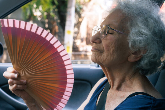 Elderly woman cooling herself with a fan while sitting in a car during a heatwave