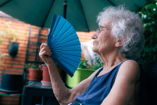 Elderly woman cooling herself with a fan while sitting on the balcony during a heatwave
