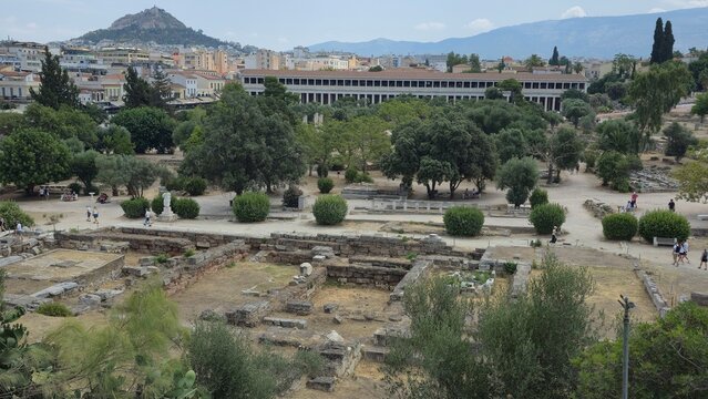 Athens, Greece - 8 July 2026. Ancient Agora with excavated foundations, tree-lined paths and the Stoa of Attalos, with Lycabettus Hill rising behind central Athens.