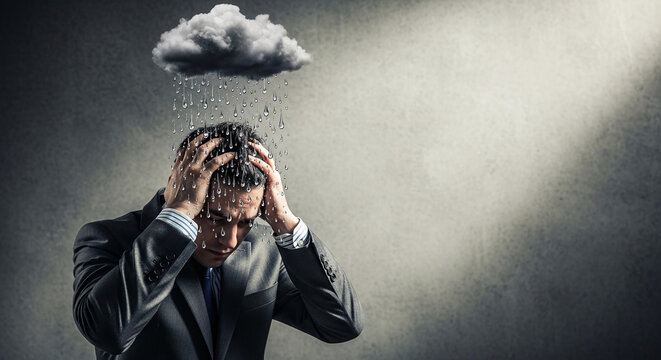 Man in suit with hands on head under a rain cloud, symbolizing stress, worry, and difficult times, perfect for business or lifestyle themes.
