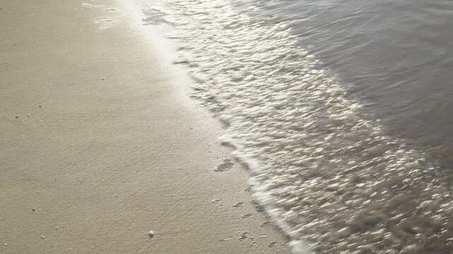 France, Valras Plage August 08, 2026 &mdash; Handheld close up shot of a gentle transparent sea wave with foam washing over wet sand texture on a beautiful beach during a peaceful sunny summer morning
