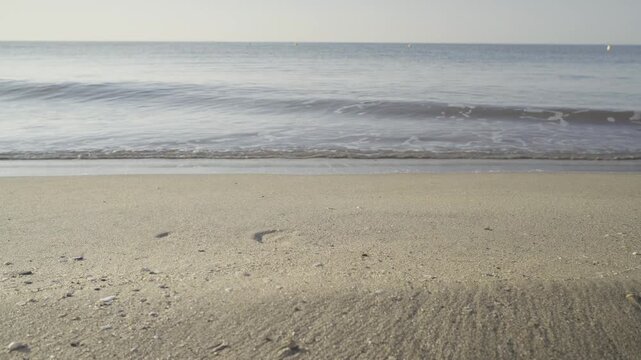 France, Valras Plage August 08, 2026 &mdash; Handheld shot of a peaceful empty sandy beach with a small sea wave coming ashore and a clear blue sky over the calm Mediterranean water horizon
