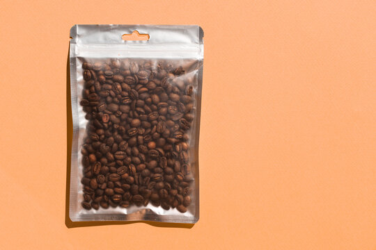 Blank craft plastic pouch mock up with coffee beans inside, transparent pack on studio background with shadow, mylar bag isolated for coffee product