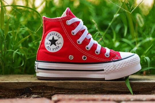 Red Converse Chuck Taylor high top sneaker rests outdoors on weathered wood.
