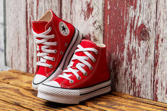 Red Converse high top sneaker pair stands against a distressed wooden wall.