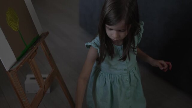Talented little girl painting a yellow tulip on easel