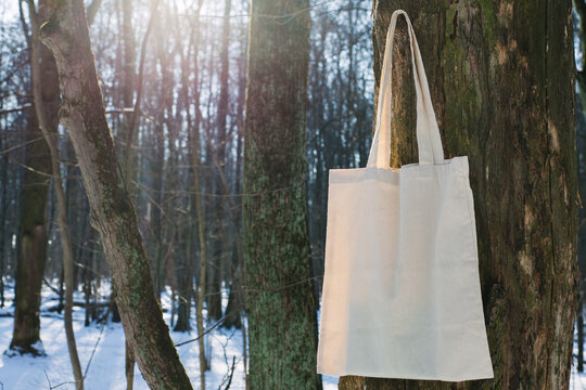 White cotton mesh bag hanging on tree branch, winter forest, sunny day background. Zero waste, no plastic, eco friendly shopping, recycling, christmas concept. Blank mockup, place for text copy space