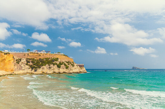 Rocky promontory cape, Cala del Mal Pas beach in El Castell Old town Benidorm city historic centre and Isla de Benidorm island background on Costa Blanca coast Mediterranean Sea in summer day, Spain