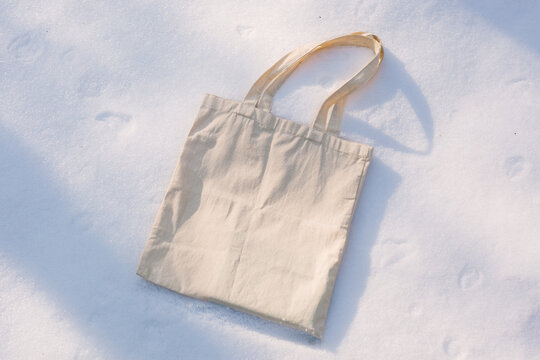 White cotton mesh bag on winter snow with fir tree branches background. Zero waste, no plastic, eco friendly shopping, recycling, christmas concept. Blank mockup, place for text. copy space flat lay