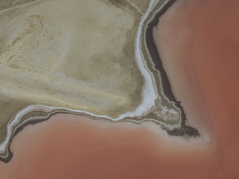 Aerial view of the pink salt pans at Salin d'Aigues-Mortes, showing the contrast between vibrant pink water and textured salt crusts in Aigues-Mortes, Occitanie, France.
