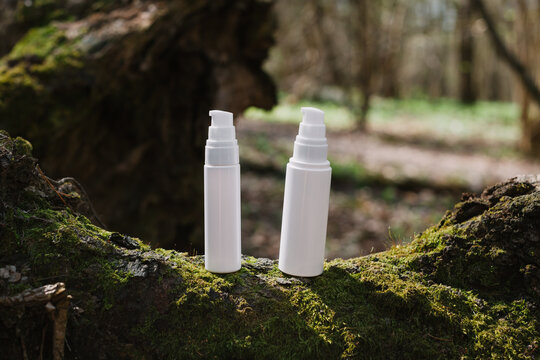 A dark and light glass serum bottle with a dropper, tree bark wood, moss. forest on a sunny day nature background. Concept of skin care, hydration, cosmetic demonstration eco-friendly product mock up