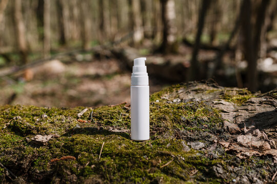 A dark and light glass serum bottle with a dropper, tree bark wood, moss. forest on a sunny day nature background. Concept of skin care, hydration, cosmetic demonstration eco-friendly product mock up