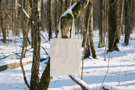 White cotton mesh bag hanging on tree branch, winter forest, sunny day background. Zero waste, no plastic, eco friendly shopping, recycling, christmas concept. Blank mockup, place for text copy space