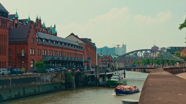 Ferry boat navigates canal in Hamburg's Speicherstadt with Elbphilharmonie and Kibbelstegbrucke background, panoramic German city sightseeing