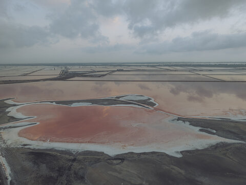 Aerial view of the pink salt pans at Salin d'Aigues-Mortes with reflective water and geometric patterns under a cloudy sky in Aigues-Mortes, Occitanie, France.
