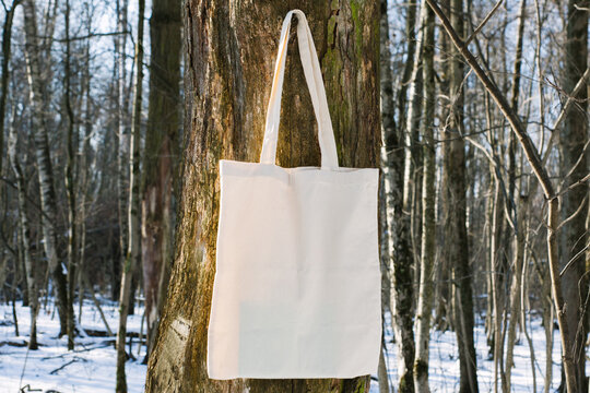 White cotton mesh bag hanging on tree branch, winter forest, sunny day background. Zero waste, no plastic, eco friendly shopping, recycling, christmas concept. Blank mockup, place for text copy space