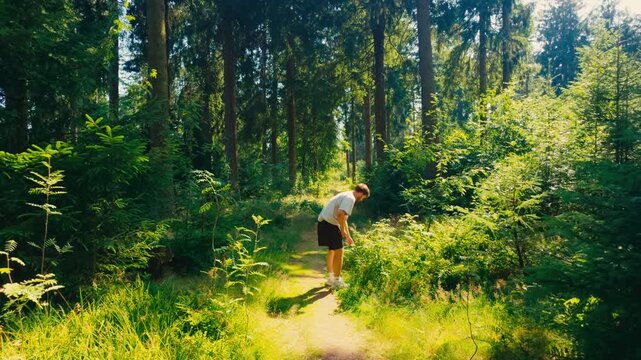 Hiker picking and smelling wild plants while walking on a sunny path in a lush green forest, exploring nature's tranquility in Taunus Forest and enjoying outdoor adventure