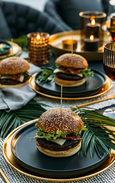 Gourmet beef burgers with sesame buns, cheese and lettuce on black plates. Elegant restaurant table setting with golden accents and burning candles. Dinner food photography concept