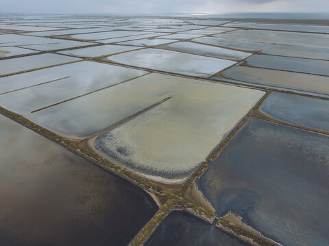 Aerial view of Le Salin de l'ile Saint-Martin de Gruissan with its geometric salt pans and varying water colors under a cloudy sky in Gruissan, Occitanie, France.