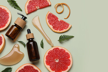 Fototapeta premium Composition with bottles of cosmetic products, facial massage tools and slices of grapefruit on green background, closeup