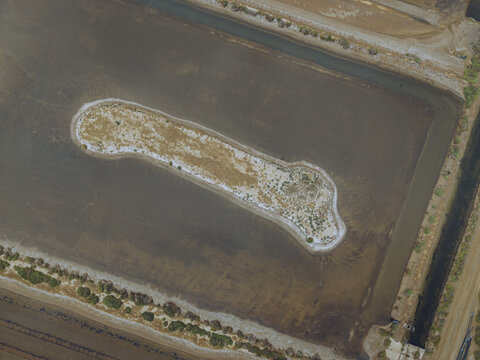 Aerial view of the salt pans at Le Salin de l'ile Saint-Martin de Gruissan, showing the distinct island shape surrounded by shallow water and salt flats in Gruissan, Occitanie, France.