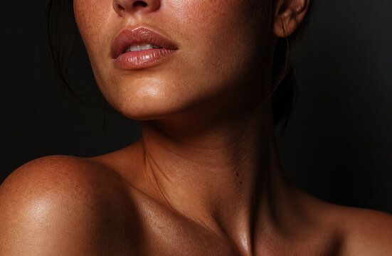 Close up tanned female lower face, glowing lips, neck, and shoulder, dark background, warm lighting, natural beauty model, skincare portrait stock photo
