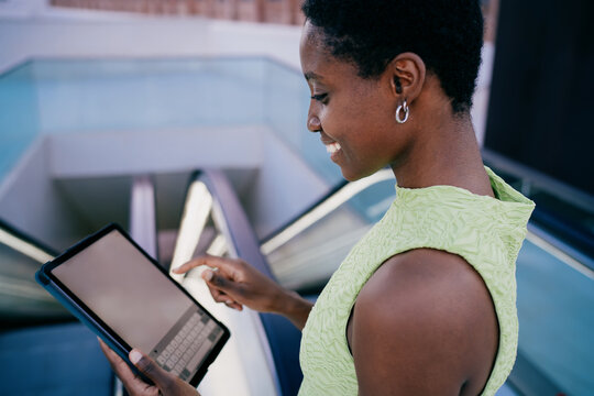 happy african american woman scrolling on tablet touch screen device. The tech-savvy black female interacting with social media platform or checking transit updates near terminal escalator