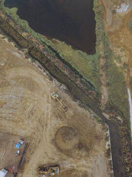 Aerial view of an excavator working at Le Salin de l'ile Saint-Martin de Gruissan, with muddy terrain and water channels in Gruissan, Occitanie, France.