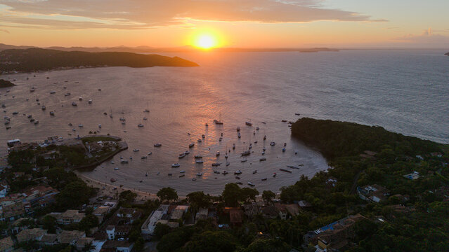 Aerial view of Praia dos Ossos at sunset, with boats anchored in the bay, surrounded by lush vegetation and buildings in Armacao dos Buzios, State of Rio de Janeiro, Brazil.