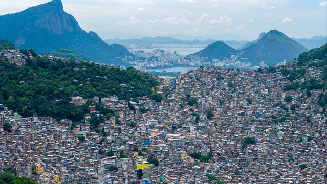 Aerial view of the dense urban landscape of Rocinha favela, featuring tightly packed houses, lush green hills, and the distant city skyline, Rio de Janeiro, Rio de Janeiro, Brazil.