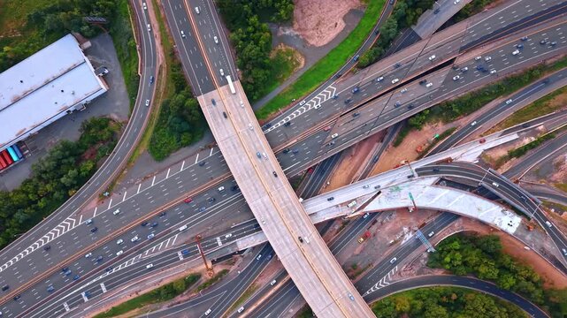 Modern complex interchange with fast running cars. Drone flight over the multi-level highway intersection surrounded by forests.