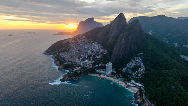 Aerial view of the Vidigal favela nestled between lush green mountains and the Atlantic Ocean during a golden sunset in Rio de Janeiro, Rio de Janeiro, Brazil.