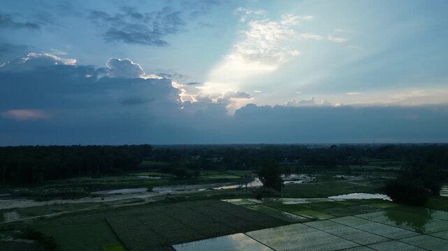 Dramatic sun rays breaking through sunset clouds over rural agricultural fields, drone footage