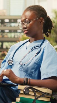 Vertical frame: The focused medical student types on a laptop in blue scrubs with a stethoscope, taking notes seated on a bench during independent study on a modern outdoor medical school campus.