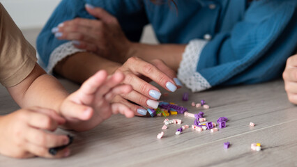 Fototapeta premium Close view of small hands and adult hands reaching toward scattered colorful building pieces on wooden floor, showing cooperative play, home learning, care, creativity, and gentle family connection