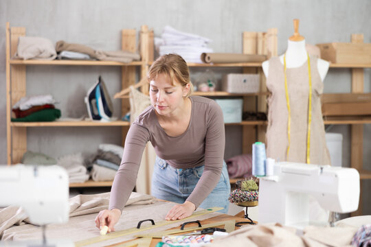 In sewing studio, professional young female dressmaker carefully drawing chalk lines across linen fabric, measuring and marking linen fabric in preparation for cutting..