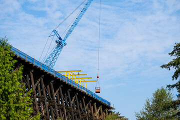Fototapeta premium Old wooden railroad train trestle construction project, blue crane holding work basket over job site, maintenance on structural framework, sunny summer day, United States 