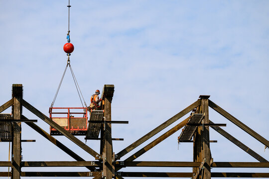 Worker in safety equipment in work on scaffolding overhead, old wood railway train trestle construction project to update structural framework, sunny summer transportation project, United States
