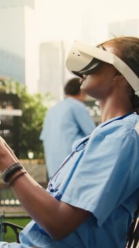Vertical screen: The medical student uses VR controllers and a headset on a wooden bench, practicing immersive healthcare learning outdoors on a sunny campus lawn in blue scrubs for medical training.