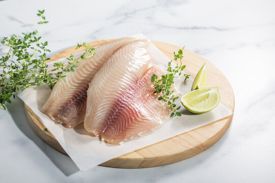 Raw fish fillet of tilapia on a cutting Board with lemon and spices.