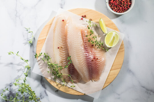 Raw fish fillet of tilapia on a cutting Board with lemon and spices.