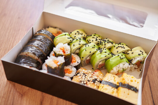  Assorted sushi rolls arranged on in a box, featuring maki rolls with salmon, tuna, tamago surimi, avocado, lettuce, cucumber and other vegetable fillings. 