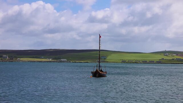 Traditional wooden Viking ship floating in clear bay waters near Lerwick Shetland Islands with green rolling hills behind