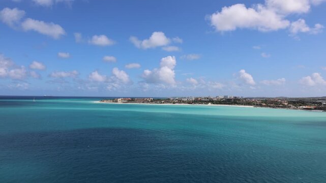 Panoramic view of the turquoise Caribbean sea, white sand beach, and coastal buildings along the shore of Eagle Beach Aruba