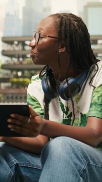 Vertical video: Women students discuss notes with a tablet while seated on campus beanbags, highlighting shared study session and project discussion, during peer tutoring, during group study.