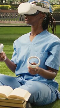Vertical aspect: The Black woman medical student wears a VR headset and raises the controllers during medical training, dressed in blue scrubs, for science education.