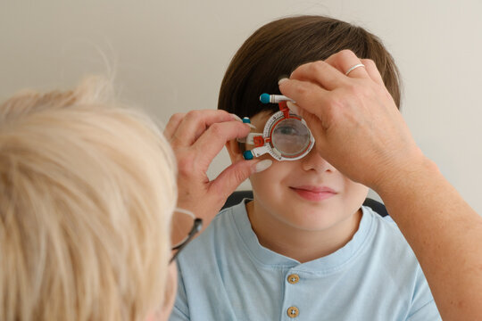 Optometrist adjusting trial frame glasses on boy during eye test in pediatric ophthalmology clinic for vision checkup.